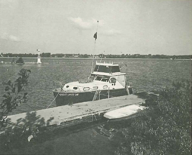 Black & white photo of a black & white boat tied up to a dock in the water