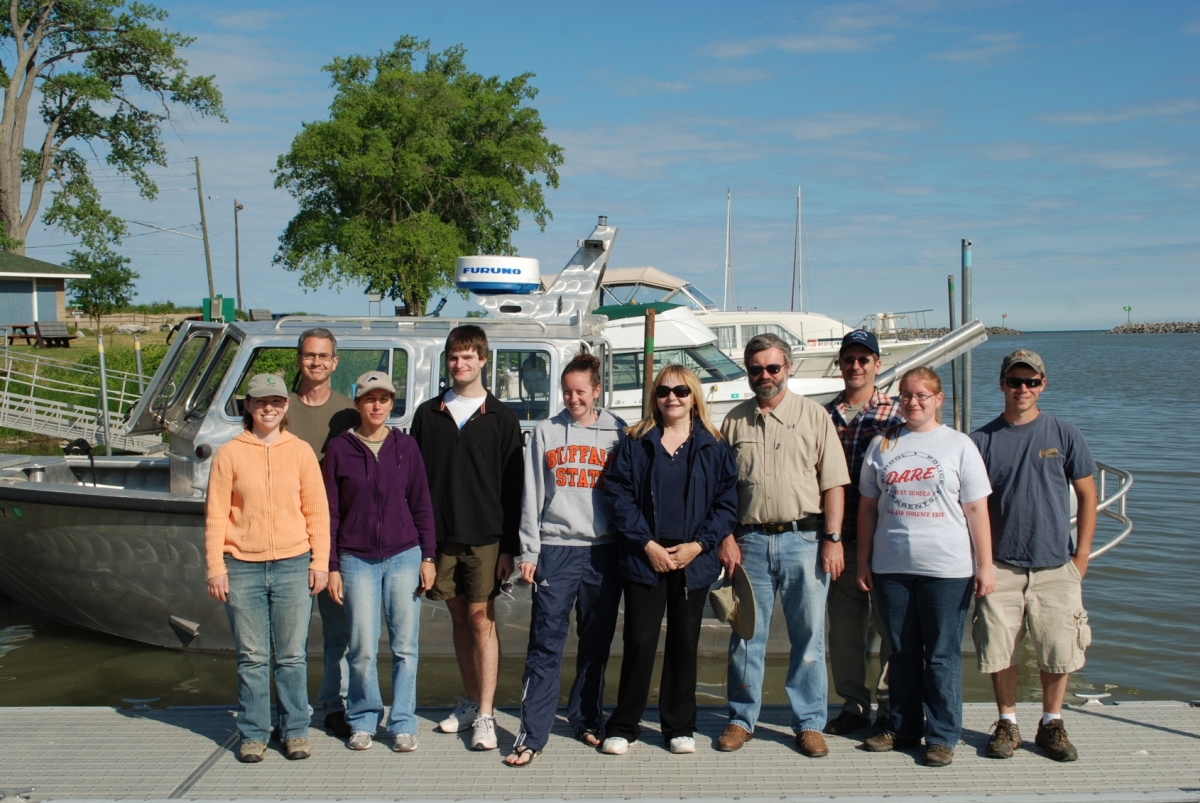 a group of people stand in front of a silver boat at a dock