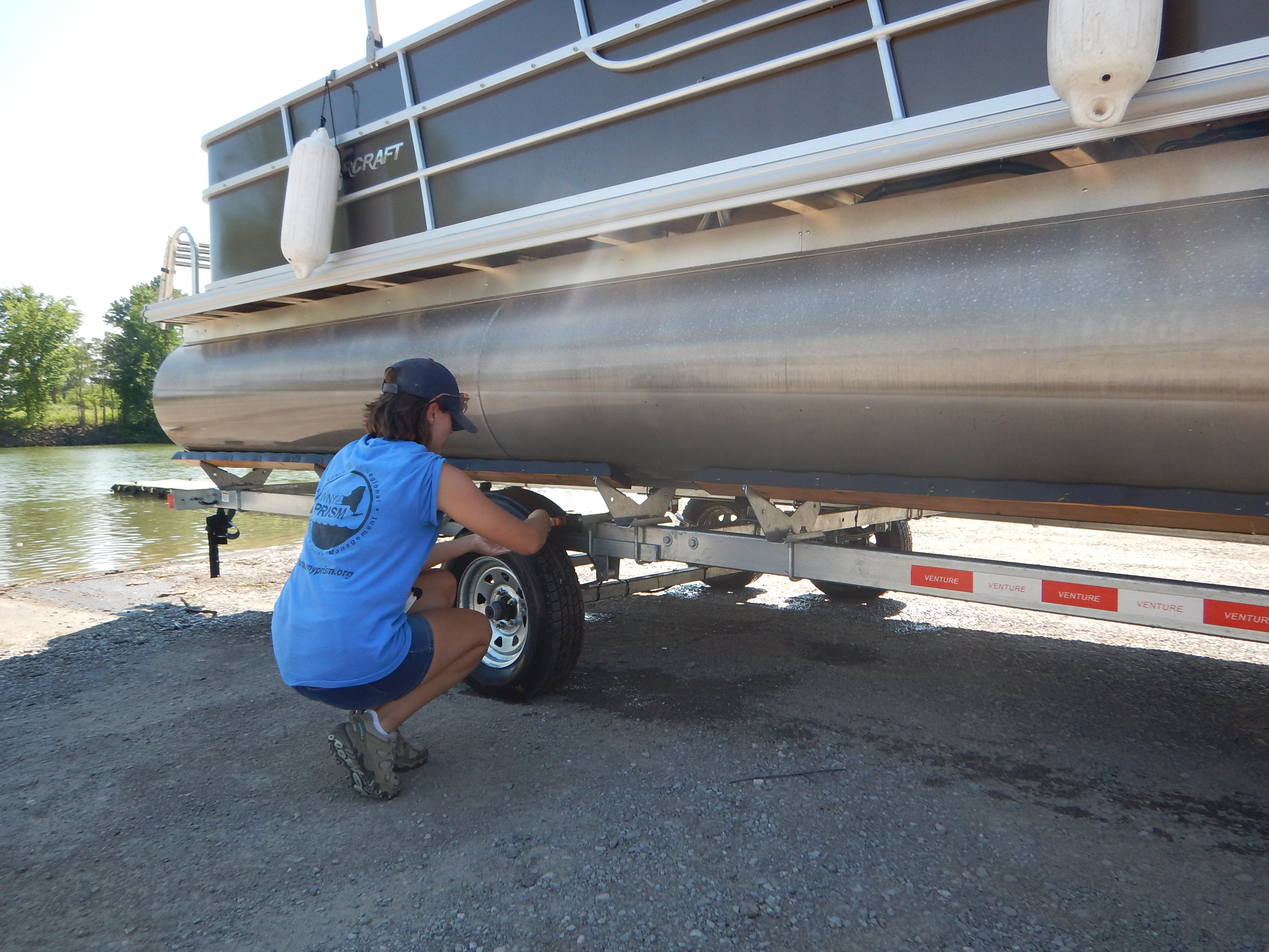 a person crouches by a boat on a trailer to inspect it