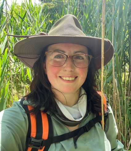 a person wearing a hat and glasses walks through tall grasses