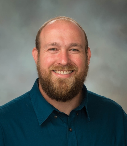 a balding person with short hair and beard wearing a blue button-down shirt