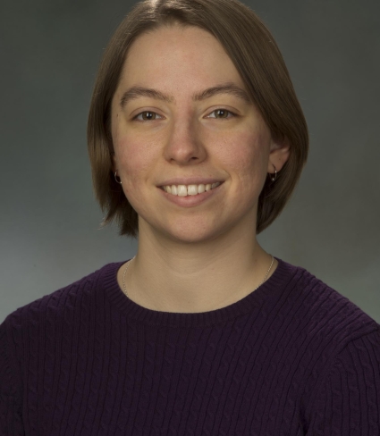 portrait of Kit Hastings, a light-skinned person with bobbed-length brown hair and brown eyes wearing a purple sweater