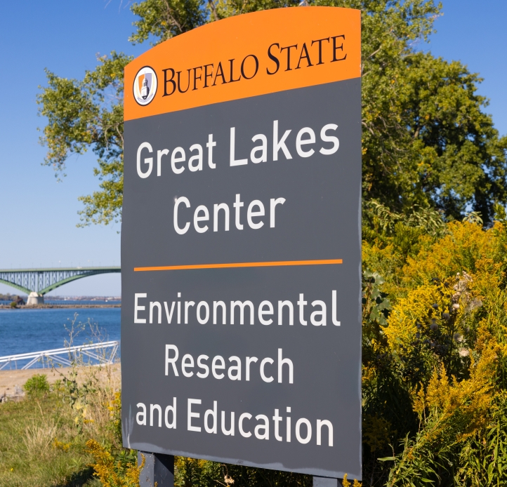 A sign for a building by a garden with goldenrod near the waterfront. "Buffalo State Great Lakes Center, Environmental Research and Education"