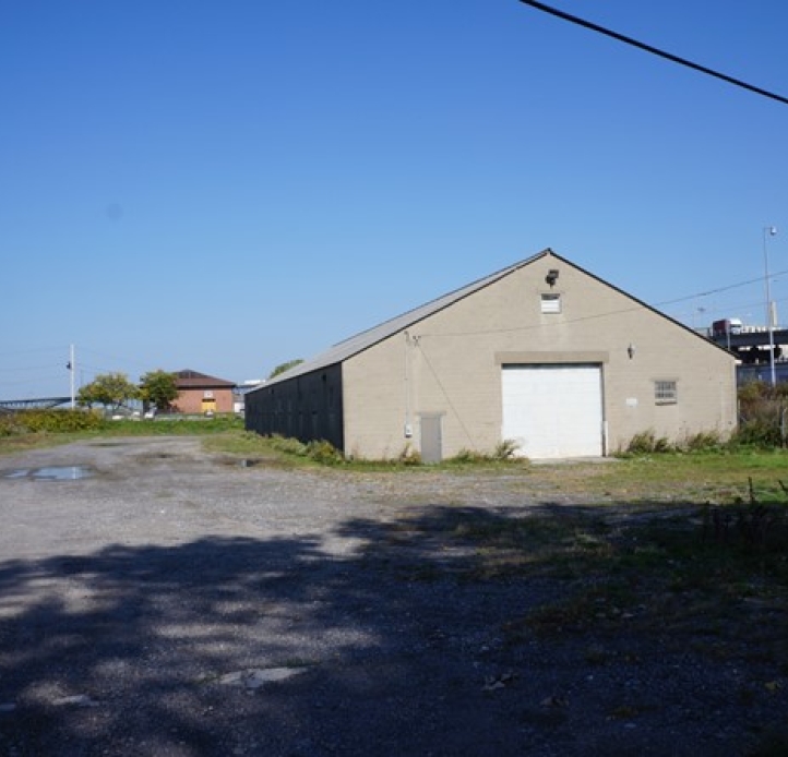 a building with a large garage door and a small person door, in a gravel lot surrounded by fencing