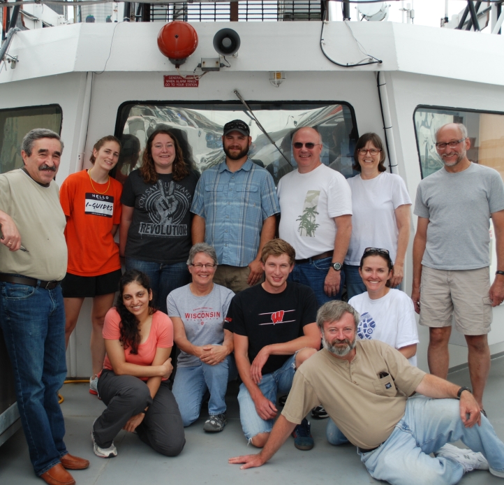 Twelve people pose for a group picture near the wheelhouseof a large boat