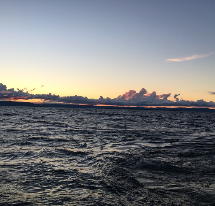 A large dark body of water at sunset with a band of clouds low on the horizon. 