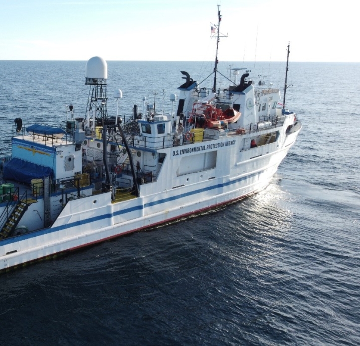 A ship on a large body of water. There are a few people on the back deck of the boat. The boat says "U.S. Environmental Protection Agency."