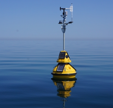 A science buoy with weather instruments on a tall mast floating on calm water