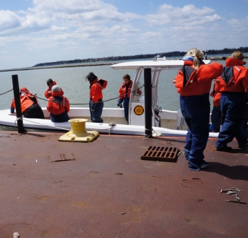 People in coldwater safety gear step on board a fiberglass boat tied up at dock