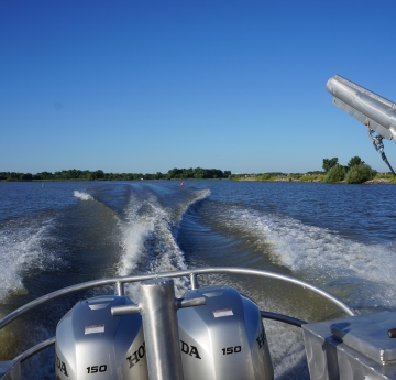 The back of a boat with two engines and a davit. The boat is throwing wake as it goes.