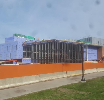 A partially constructed building that has walls enclosing part of it, a steel frame surrounding a steel globe, and some windows on both parts of the building.