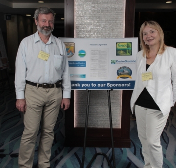 two people stand on either side of a poster on an easel. The poster says "thank you to our sponsors!"