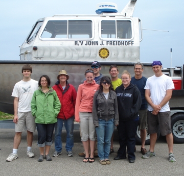 Ten people stand in front of a boat on a trailer. The boat is named "R/V John J. Freidhoff."