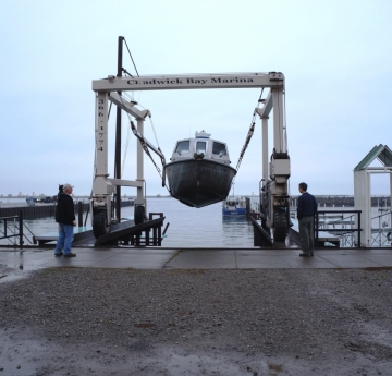 A metal frame in a marina holding a boat aloft over the water, with two people watching