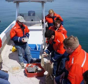 People on a boat looking at equipment. One holds a net