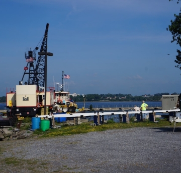 A tug and a barge with a crane approach a dock