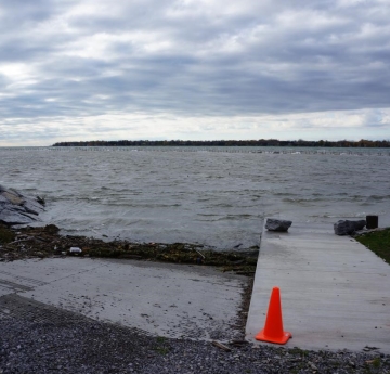 A ramp leading down the water is mostly submerged by waves. There is a line of weeds, wood, and garbage at the waterline.