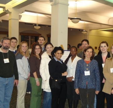 twelve people stand for a group photo inside a hall, with some posters on easels in the background