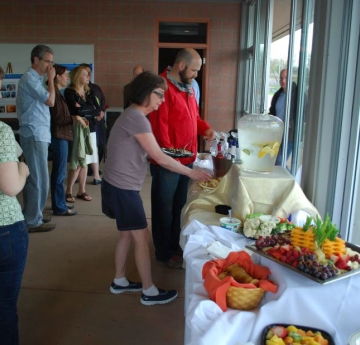 People grab food from a buffet table set up along a wall of windows
