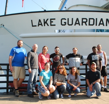 A group of people posing for a picture in front of a ship called Lake Guardian.