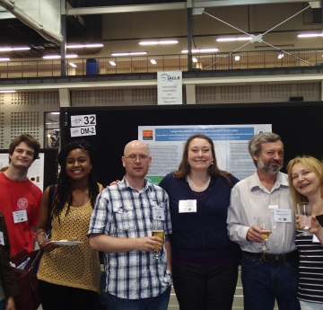 Eight people pose for a picture in front of an academic poster on a board at a conference