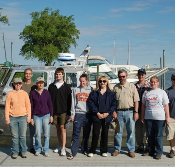 Ten people stand on a dock in front of a boat