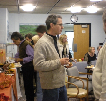 People talking, holding snacks. There is a fall-themed table with food to the left.