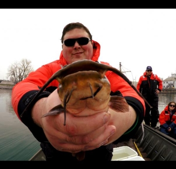 A student on a boat holds up a brown bullhead to the camera. There are students in a second boat in the background.