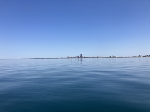 A very calm large lake with a city in the distance, and no clouds in the sky.