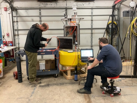 Two people working in a garage to assemble a buoy and test electrical equipment and instruments.