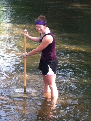 A person wading in a shallow stream with a rectangular net on a pole under the water