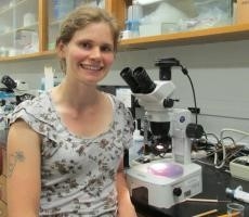 A person sits next to a microscope in a lab.