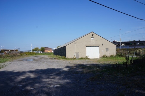 a building with a large garage door and a small person door, in a gravel lot surrounded by fencing