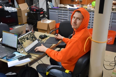 A person in a hoodie sits working on a laptop in a lab