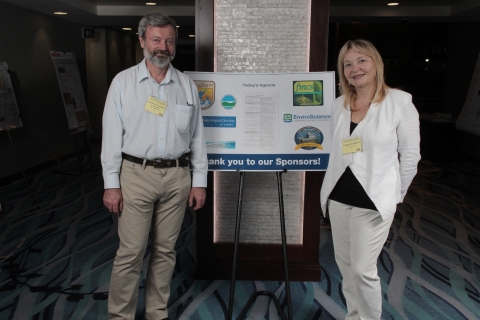 two people stand on either side of a poster on an easel. The poster says "thank you to our sponsors!"