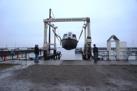 A metal frame in a marina holding a boat aloft over the water, with two people watching