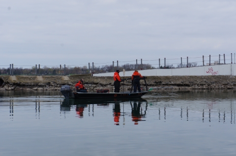 Three people on a boat by a breakwall.