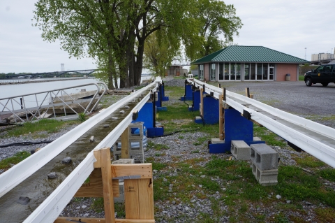 Two long narrow gutters propped up in a yard. There is water flowing through each, and algae growing in the water.