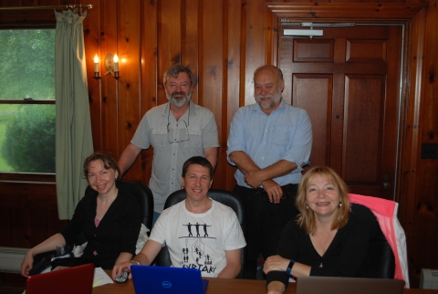 Five people posing for a picture in an office room. Three are seated at a table while two stand behind them.