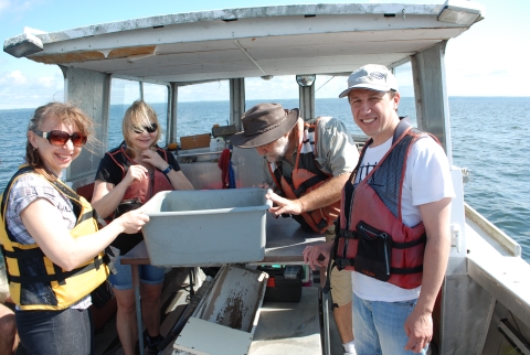 Four people on a boat standing around a tub on a table. One person is looking into the tub.