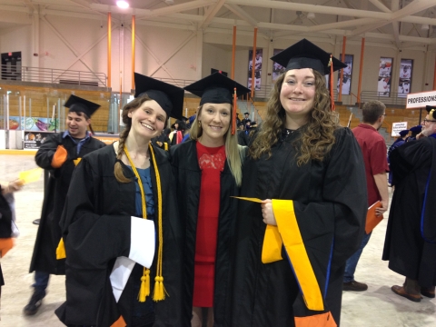 Three people wearing caps and gowns in a gymnasium.