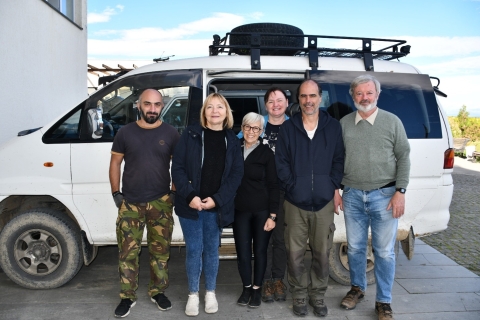 Six people smile and pose next to a van