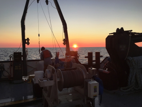 A person working on a large boat at sunrise.