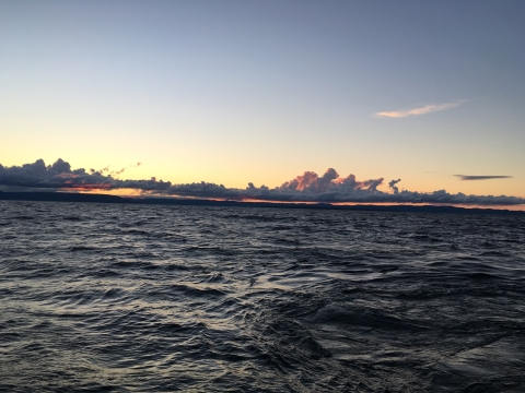 A large dark body of water at sunset with a band of clouds low on the horizon. 