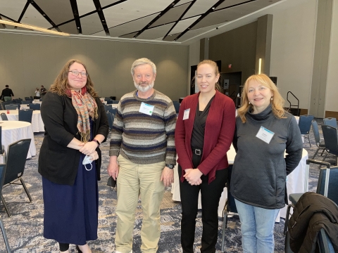 Four people pose for a picture in a large, mostly empty conference hall.