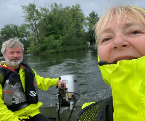 Two people in a selfie while one steers and outboard motor on a boat in the water.