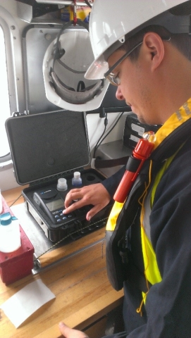 A person in a hard hat and life jacket uses water testing equipment on a work bench.