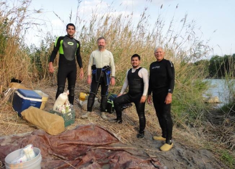 Four people in wetsuits stand on the bank of a river