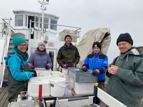 Five people in winter coats and hats work on the deck of a large boat