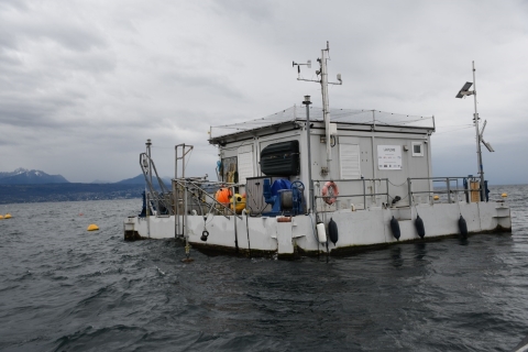 A floating platform on a large lake with a building above the water level. There are scientific instruments aboard.